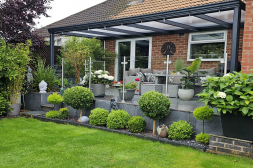 Klassieke antraciete terrasoverkapping met veel planten en een polycarbonaat dak Klassieke antraciete terrasoverkapping met veel planten en een polycarbonaat dak